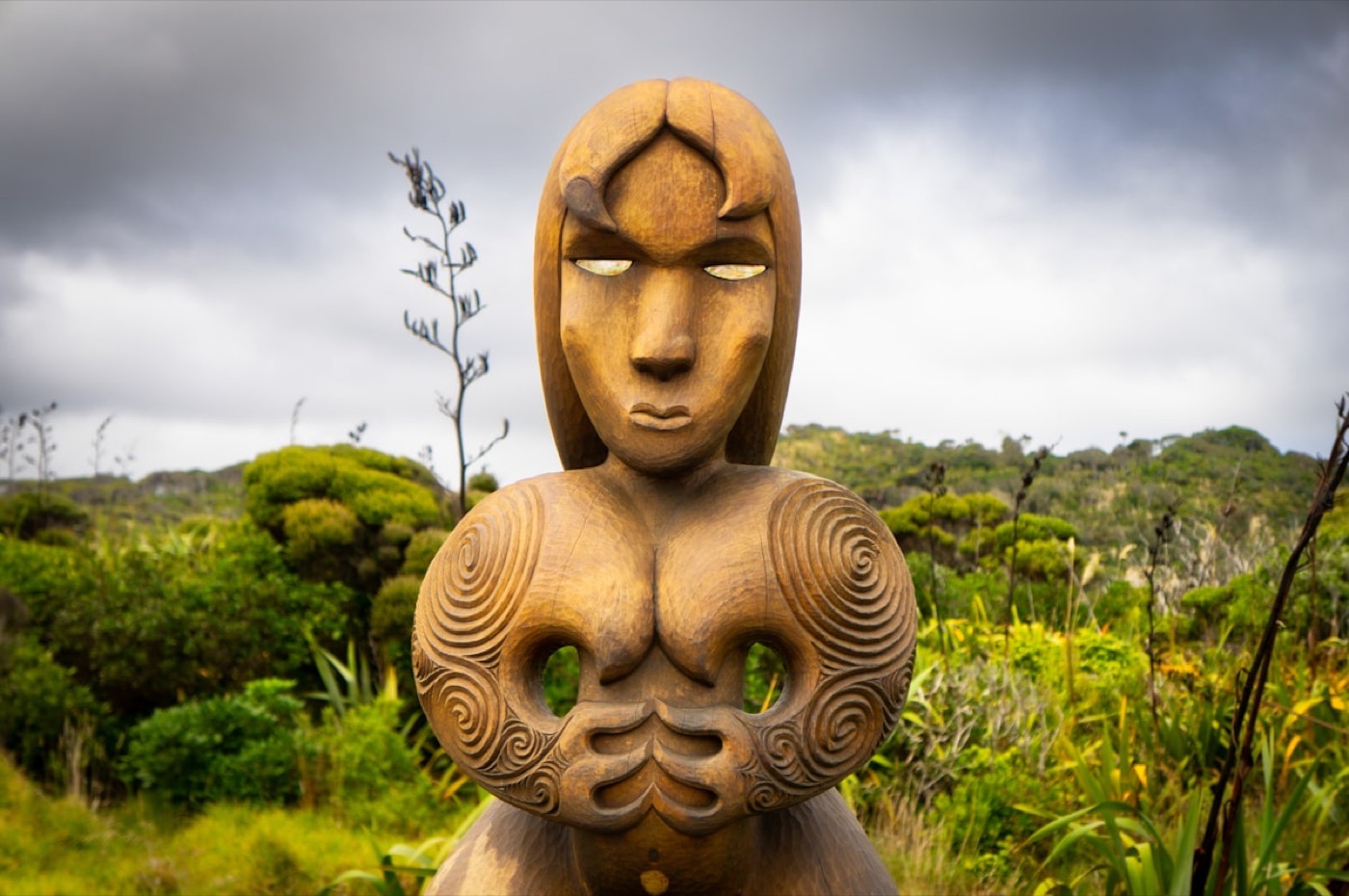 Carved wooden pou whakairo standing among native bush
